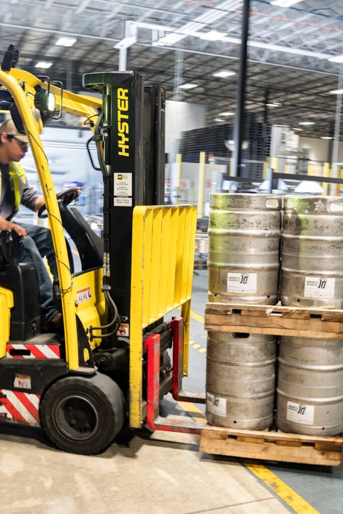 Forklift operator in warehouse moving beer kegs for distribution.